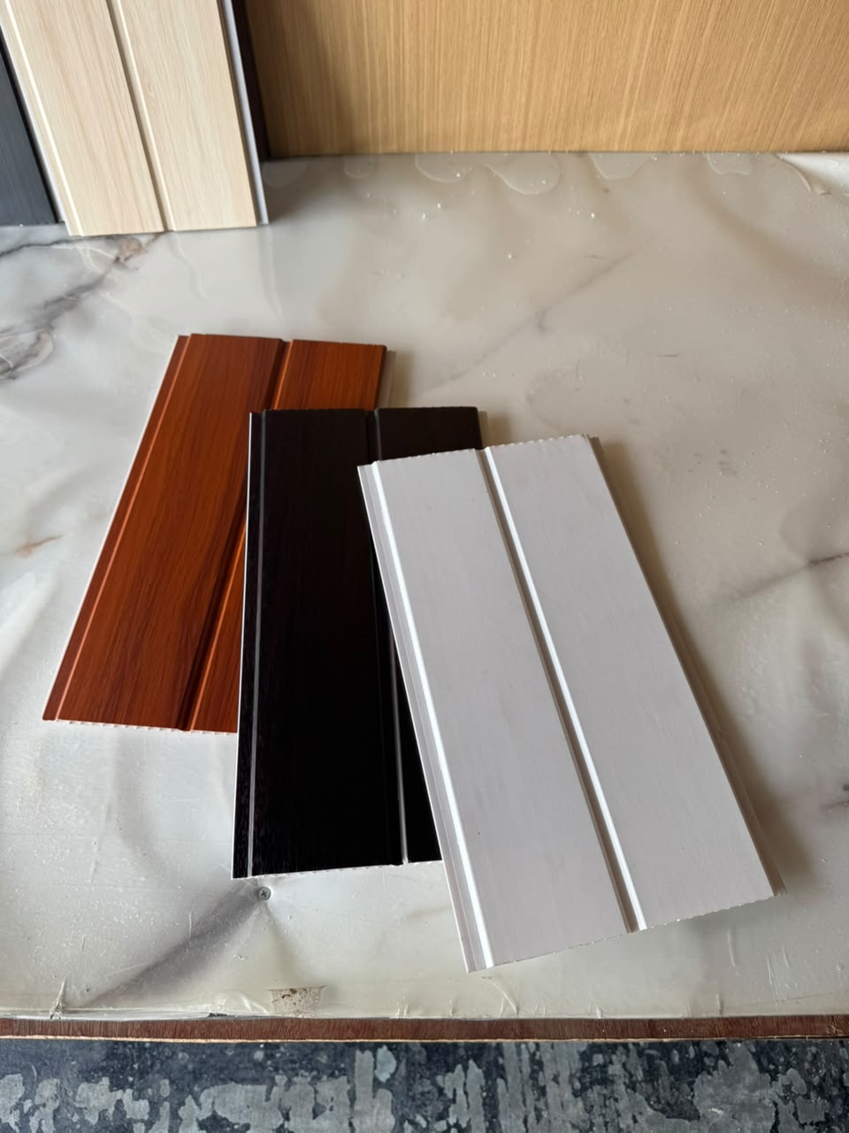 Sampel panel siling PVC 105 Alder, 103 Walnut dan 108 White di atas kaunter marmar