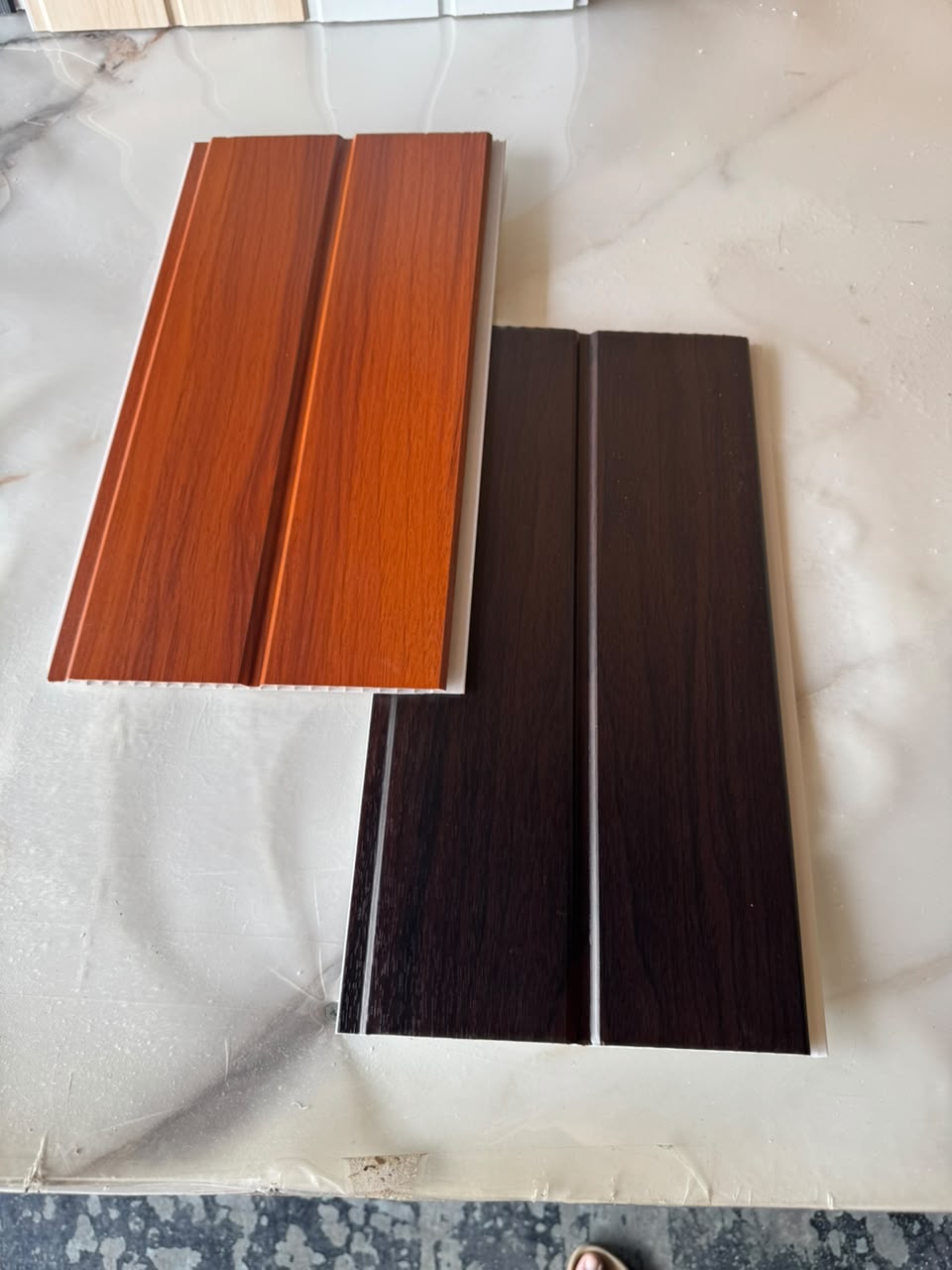 105 Alder and 103 Walnut woodgrain PVC ceiling panel samples side by side on a marble counter